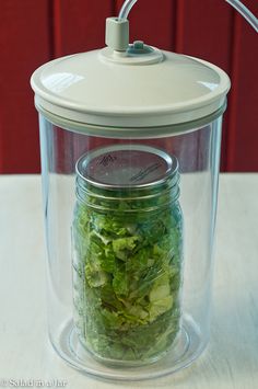 a glass jar filled with lettuce sitting on top of a table