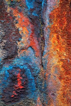 an abstract painting with orange, blue and red colors on the side of a rock