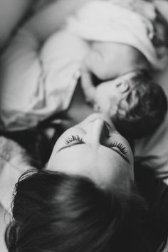 a woman laying on top of a bed next to a baby