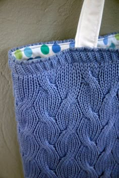 a blue knitted tote bag hanging on a wall with polka dots around it