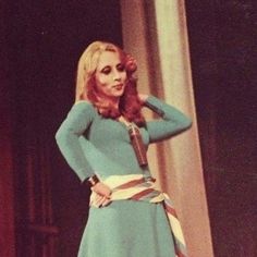 a woman in a blue dress is standing with her hands on her hips