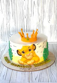 a lion cake with a crown on top is sitting on a wooden table next to a white fence