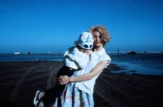 a woman holding a child on the beach with water in the backgroung