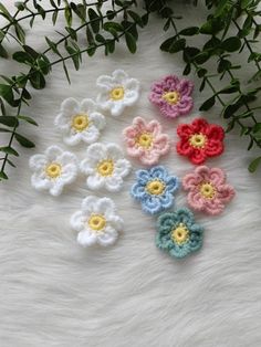 small crocheted flowers sitting on top of a white fur covered floor next to green leaves