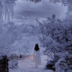 a woman in a white dress is walking through the woods with snow on her feet