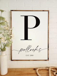 a wooden sign with the letter p on it next to a white vase and flowers