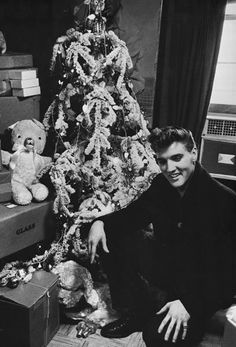 a black and white photo of a man sitting in front of a decorated christmas tree