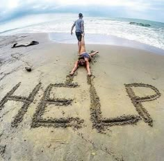 a man standing on top of a sandy beach next to the words help written in sand