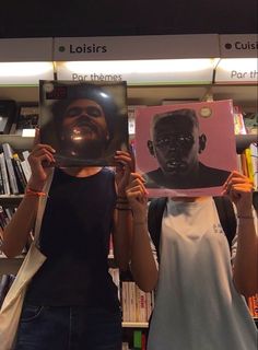 two people holding up posters in front of bookshelves, one with a man's face on it