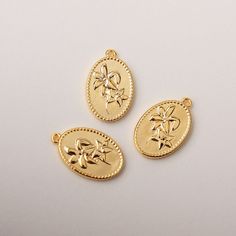 three gold pendants with flowers on them sitting on a white surface, one in the shape of an oval