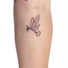 a small tattoo on the leg of a woman with a key and dragonfly attached to it