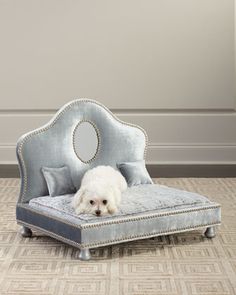 a small white dog laying on top of a blue bed with silver trimmings