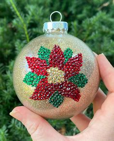 a hand holding a christmas ornament with red, green and yellow beads on it