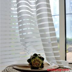 an artichoke sitting on top of a plate in front of a window with white curtains