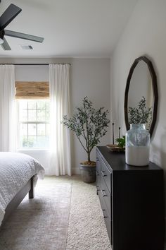 a bedroom with a bed, dresser and ceiling fan in front of a large window