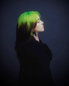 a woman with bright green hair and piercings on her ear looking off into the distance