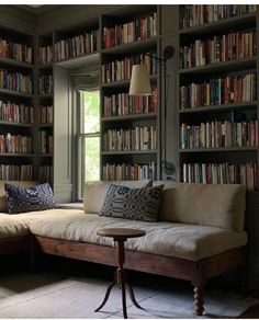 a living room filled with lots of books on top of a book shelf next to a window