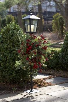 a lamp post with red berries on it in front of some bushes and shrubbery