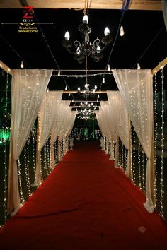 a red carpeted aisle with white drapes and lights on the ceiling is lit up by chandeliers