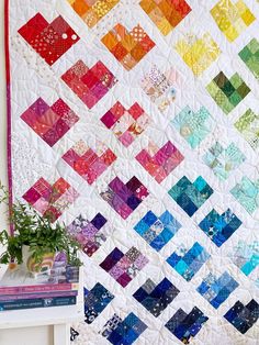 a multicolored quilt is displayed on a table next to a potted plant