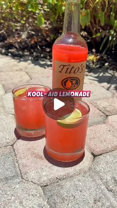 two glasses filled with red liquid sitting on top of a stone floor next to a bottle