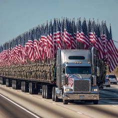 a large semi truck driving down a highway with american flags on the side of it