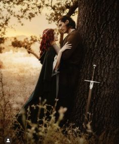 a man and woman standing next to each other in front of a tree with swords