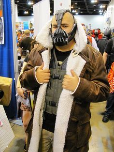 a man wearing a mask and jacket with his hands in his pockets at a convention