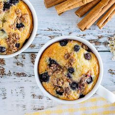 two mugs filled with blueberry muffin next to cinnamon sticks and oats