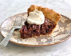 a piece of pie with whipped cream on top sits on a plate next to a fork