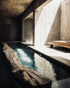 a wooden bench sitting next to a swimming pool in a room with concrete walls and flooring