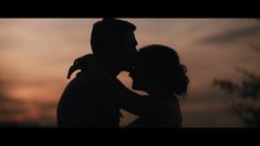 the silhouette of a man and woman embracing each other in front of an evening sky