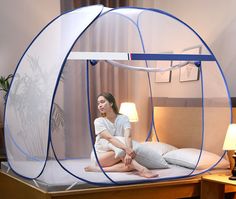 a woman sitting on top of a bed in a room with a mosquito net over it