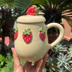 a hand holding a ceramic teapot with strawberries on it