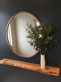 a mirror on the wall above a wooden shelf with a vase and greenery in it