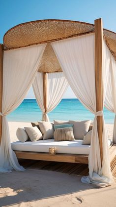 an outdoor bed with white drapes and pillows on the beach