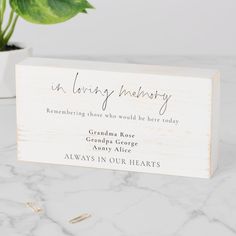 a wooden business card with the words in loving memory on it next to a potted plant