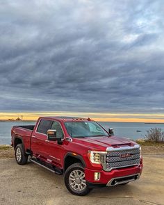 a red truck is parked on the side of the road near the water with dark clouds in the background