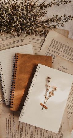 three notebooks with flowers sitting on top of an open book next to each other