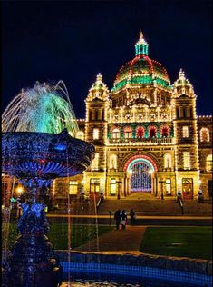 an ornate building lit up at night with lights on the buildings and fountains in front