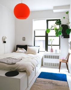 a bedroom with a bed, rugs and plants in the window sill area