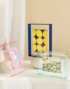 three different colored frames sitting on top of a white table next to a vase with flowers in it