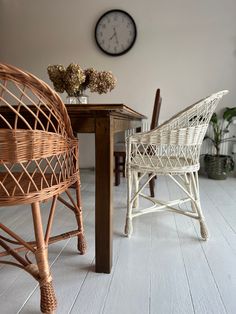 two wicker chairs sitting at a table with a clock on the wall behind them