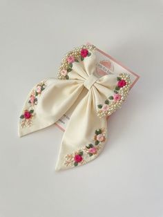 a white bow with pink flowers and pearls on the end is laying on top of a card