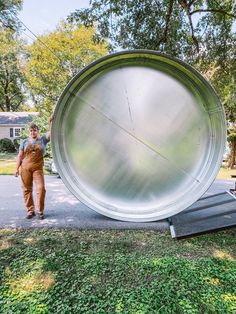 a man standing next to a large metal object on top of a grass covered field