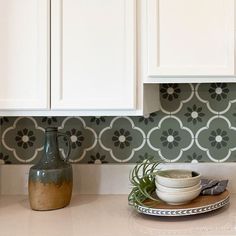 a kitchen counter with white cabinets and green tile backsplashing, including a bowl on a plate