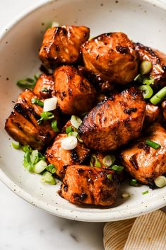 a white bowl filled with grilled chicken and green onions on top of a table