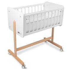 a white crib with wooden legs and wheels on the bottom, in front of a white background