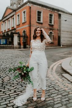 a woman standing in the middle of a cobblestone street with her hands on her head