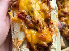 a hand holding a hot dog with cheese and chili on it's buns